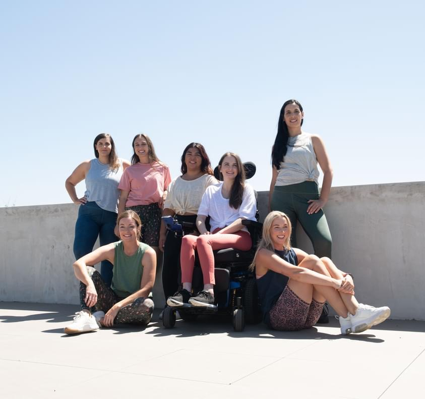 A group of women pose naturally on a rooftop with blue sky. They are all wearing various Bod By Finch activewear and Tayla is in her black electric wheelchair.