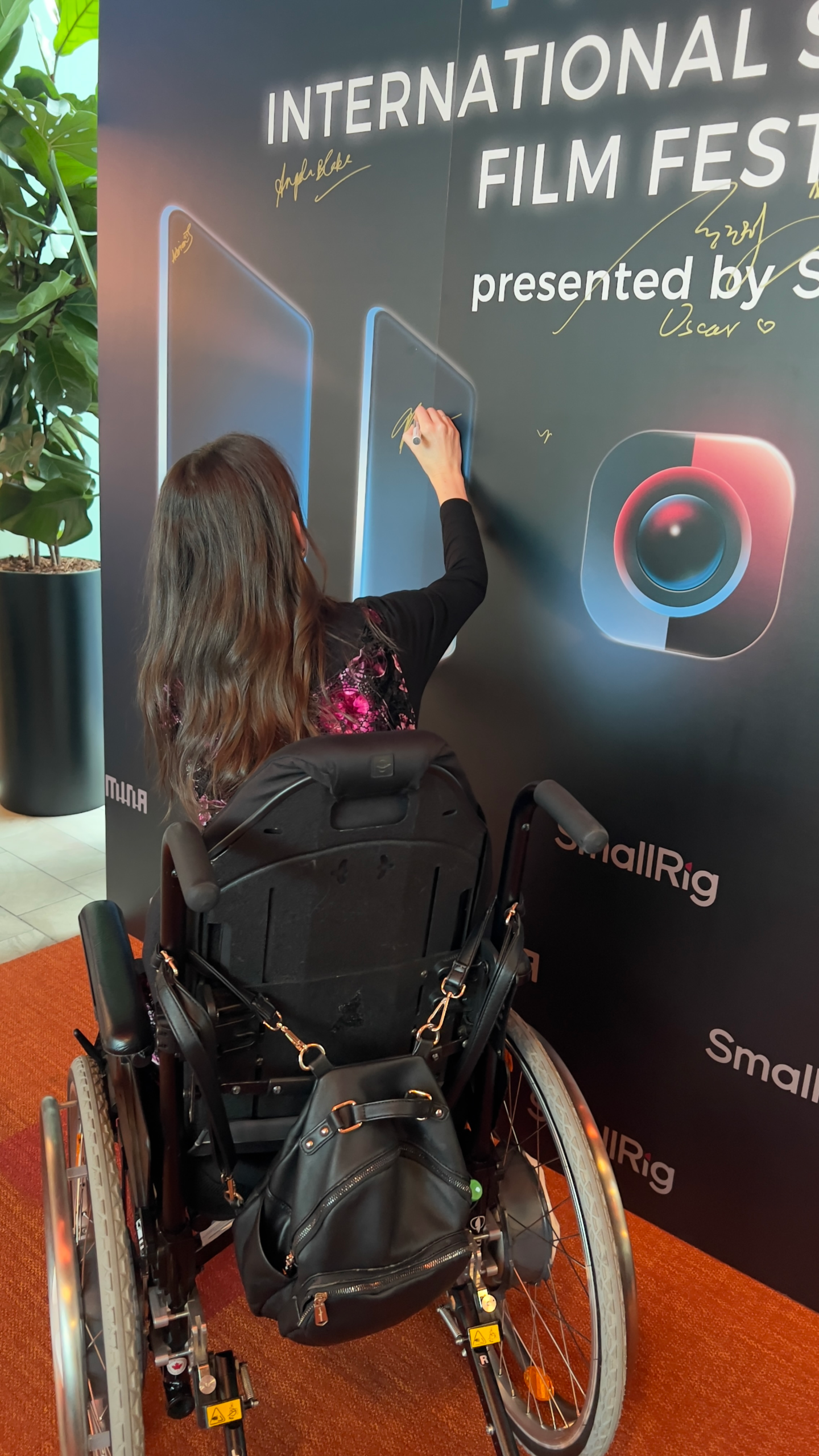Tayla is in here wheelchair on a red carpet signing a film festival wall. Text reads: International Film Festival.